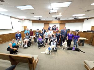 A group of people in a courtroom, some seated in wheelchairs, accompanied by service dogs.