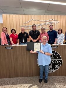 A group of people standing behind a wooden counter, with one person in front holding a certificate.