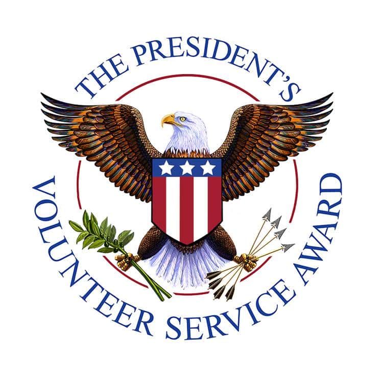 The President's Volunteer Service Award logo featuring a bald eagle with wings spread, holding an olive branch in one talon and arrows in the other, and a shield on its chest, encircled by the text "The President's Volunteer Service Award."