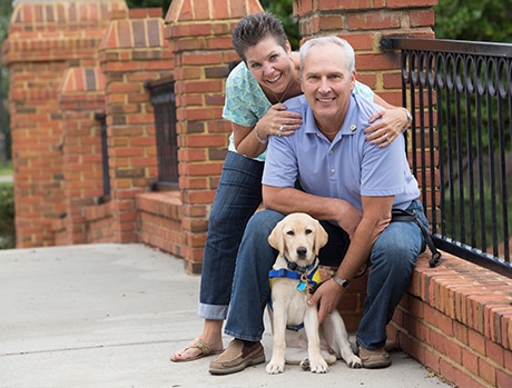 A couple posing happily with a Labrador puppy on a brick walkway.