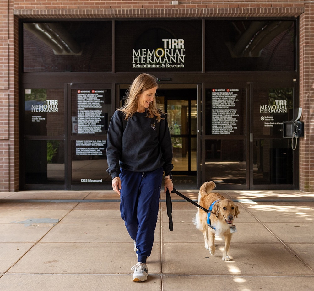 A woman walking a dog on a leash outside the TIRR Memorial Hermann Rehabilitation & Research building.