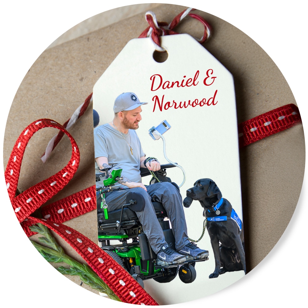 Gift tag with a man in a wheelchair and a service dog; text reads "Daniel & Norwood."