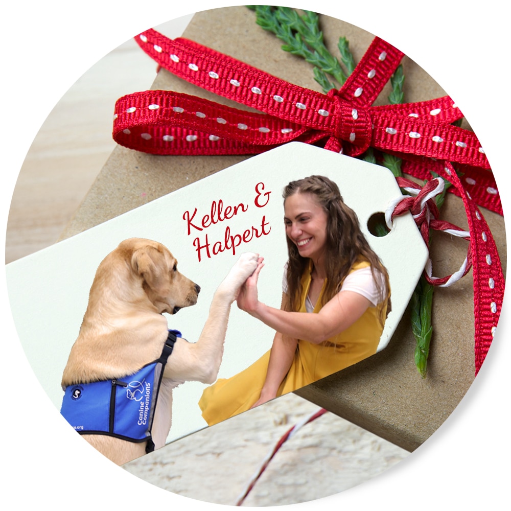 A gift tag with a woman high-fiving a service dog, labeled "Kellen & Halpert," attached to a present with red ribbon.