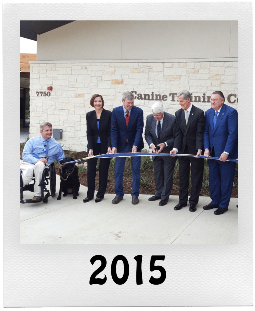 A group of people performing a ribbon-cutting ceremony in front of a building marked "Canine Training Center" in 2015.