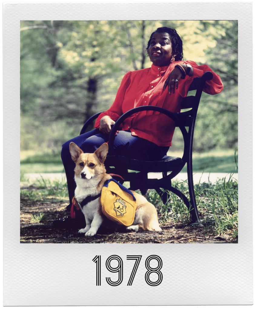 A person in a red blouse sits on a bench beside a Corgi wearing a yellow backpack labeled "D.A.R.E.", with "1978" written below.