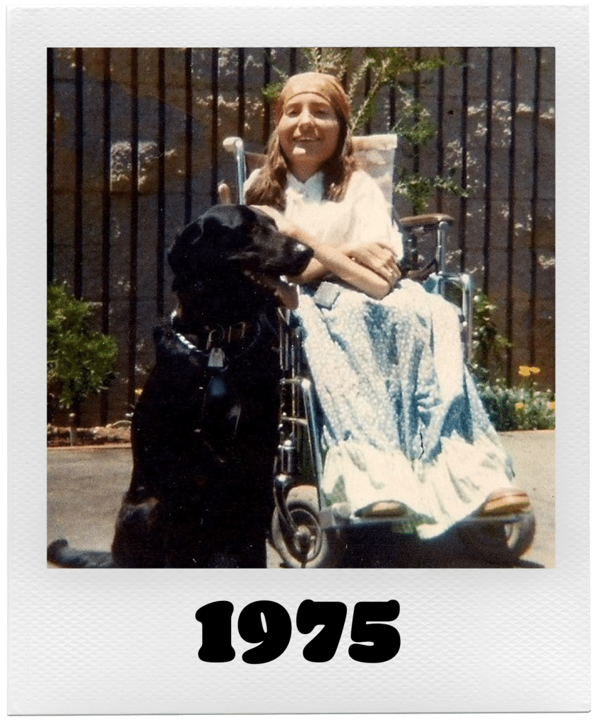 A woman sitting in a wheelchair next to a black dog in 1975.