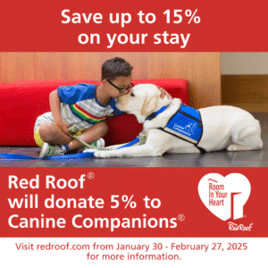 A young child wearing glasses is sitting on the floor and gently touching the nose of a large, friendly-looking yellow dog wearing a blue vest that says "Canine Companions." In the background, there is a red couch and wooden paneling. The image includes promotional text related to discounts and donations to Canine Companions by Red Roof.