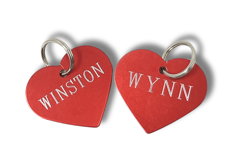 Two red heart-shaped tags with silver lettering reading "WINSTON" on one tag and "WYNN" on the other, both attached to metal rings.