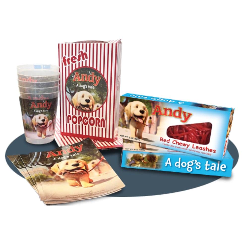 A collection of promotional items for the movie titled 'Andy: A Dog's Tale', including a popcorn bag with red and white stripes, cups featuring a dog's image, packages labeled 'Red Chewy Leashes', and printed brochures, all arranged on a circular blue background.