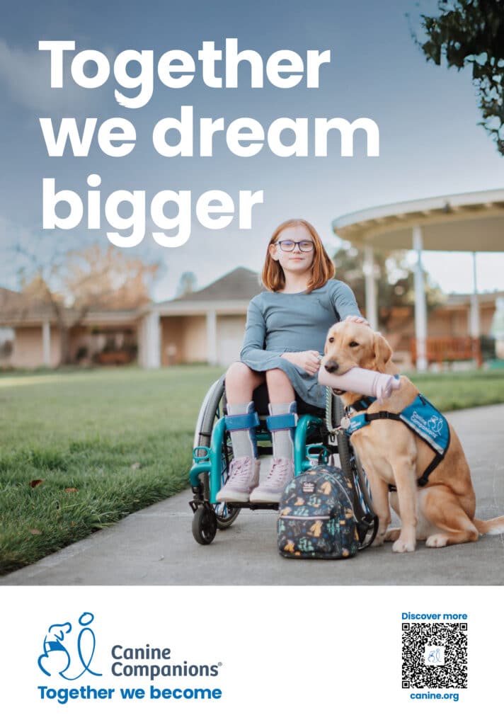 A young girl sitting in a wheelchair with a service dog beside her, both looking at the camera. The girl has short, reddish-brown hair and wears glasses, accompanied by a backpack with a colorful pattern. The background features a grassy area and a building with a covered patio. The text above reads, 'Together we dream bigger.'