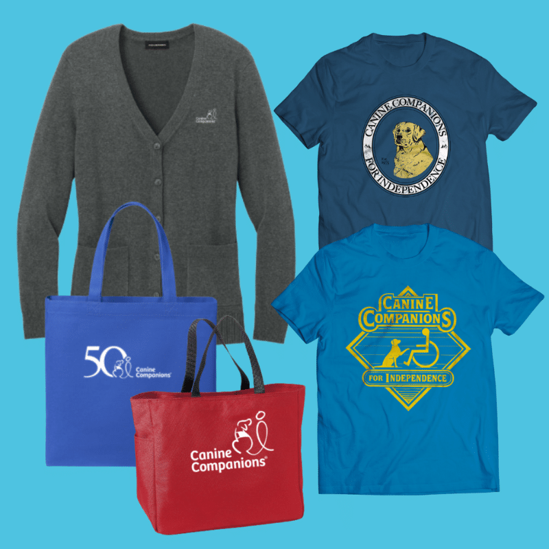 A collection of merchandise featuring Canine Companions: a gray cardigan, two blue t-shirts with different designs including a logo and a service dog image, and two tote bags—one blue with a logo for the 50th anniversary, and one red with a Canine Companions logo—all displayed against a light blue background.
