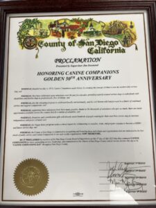 A proclamation from the County of San Diego, honoring Canine Companions on their 50th anniversary, featuring decorative illustrations and signed by Supervisor Jim Desmond and other board members.