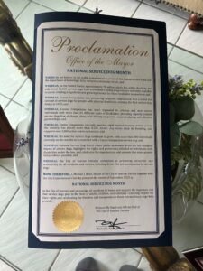 A formal proclamation document from the Office of the Mayor declaring September 2025 as National Service Dog Month, highlighting the role of service dogs in aiding individuals with disabilities and the work of Canine Companions. The proclamation includes a gold seal and the signature of Mayor Michael J. Ryan, along with a detailed explanation of the organization’s mission and achievements.