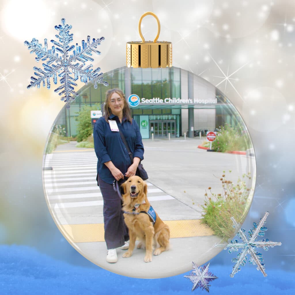 Person standing outside Seattle Children's Hospital inside a decorative glass holiday ornament graphic, holding a leash for a seated golden retriever wearing a blue service-dog vest, with large sparkly snowflakes around the bauble.