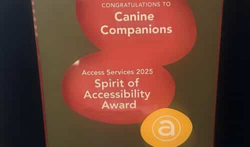 Award poster reading “Congratulations to Canine Companions” and “Access Services 2025 Spirit of Accessibility Award” on a dark green background with red overlapping shapes and a small yellow circular 'a' logo at the bottom.