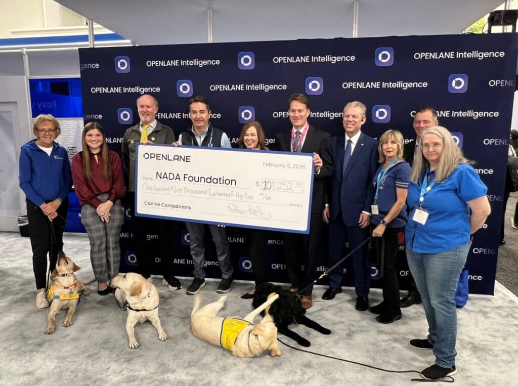 People holding an oversized OPENLANE check to NADA Foundation while four service dogs in yellow vests lie at their feet.
