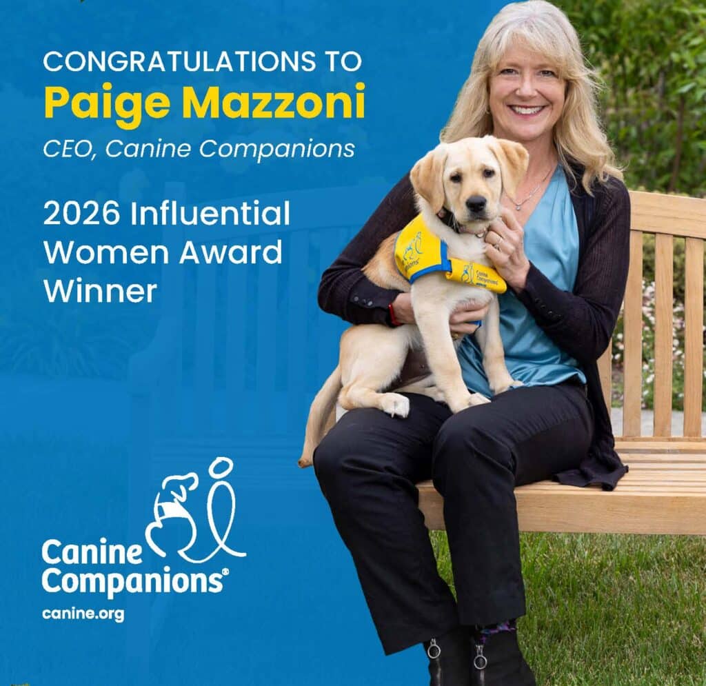 Canine Companions CEO Paige Mazzoni sits with a yellow labrador puppy wearing a yellow vest