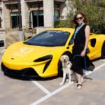 Woman standing with a service dog beside a bright yellow Canine Companions sports car