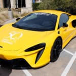 Bright yellow McLaren sports car with Canine Companions logo parked outdoors