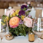 Floral centerpiece with pink, peach, yellow, and purple flowers on a decorated dining table