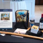 Auction display with a New Mexico trip, balloon-themed items, wine, jewelry, and a wooden walking stick on a table