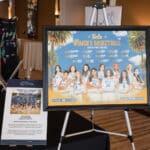 Framed UCLA women’s basketball poster on an easel beside a donation sign at a Canine Companions event