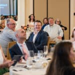 Guests seated at a formal banquet listen at round tables in a bright event room