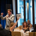 Auctioneer speaking at a fundraising event while guests bid at a table