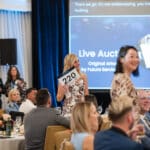 Woman holding auction paddle at a Canine Companions fundraising event in a banquet room