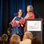 Woman in a wheelchair receives a pink therapy dog plush onstage at a Canine Companions event