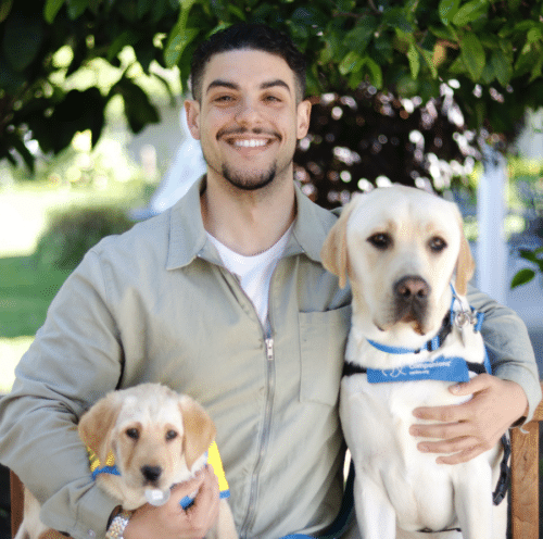 Man seating with service dog and puppy in training