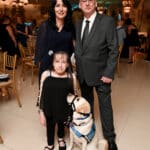 Girl with a service dog in a blue vest stands with two adults at a formal indoor event