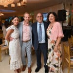 Four adults pose together at a formal indoor event under chandeliers