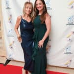 Two women pose on a red carpet in front of a Canine Companions backdrop