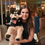 Woman smiling and holding a plush dog puppet at an indoor event