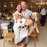 A smiling couple holds two Canine Companions dog puppets at a formal event