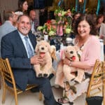 Two smiling guests at a banquet hold plush puppy dogs while seated at a decorated table