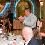 People seated at a formal banquet applaud a man standing at the table