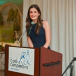 Woman speaking at a Canine Companions podium during an indoor event