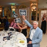 People at a fundraising dinner hold up bidding paddles at a table