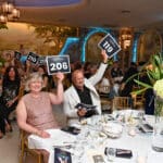Auction guests at a Canine Companions fundraiser raise bid cards at a banquet table