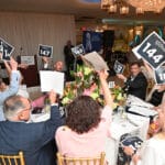 Auction bidders raising paddle signs at a Canine Companions fundraising event indoors