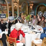 Guests at a gala raise auction paddle signs around a decorated banquet table