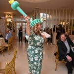 Woman in a green floral dress wearing a turquoise Statue of Liberty crown and torch at a formal event