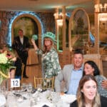 Woman wearing a Statue of Liberty crown stands at a banquet table during an indoor fundraising event