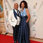 A smiling couple pose on a red carpet in formal wear before a Canine Companions backdrop