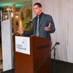 Man speaking at a Canine Companions podium during an indoor event