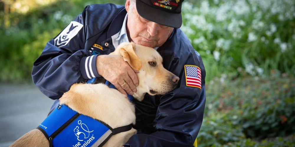 Ron in Navy Seabee hat hugging service dog Holiday